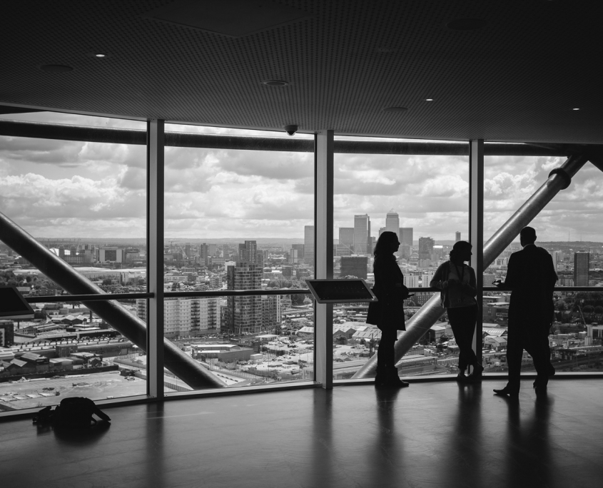 Black and white photo of three people in silhouette in an empty office overlooking a city.