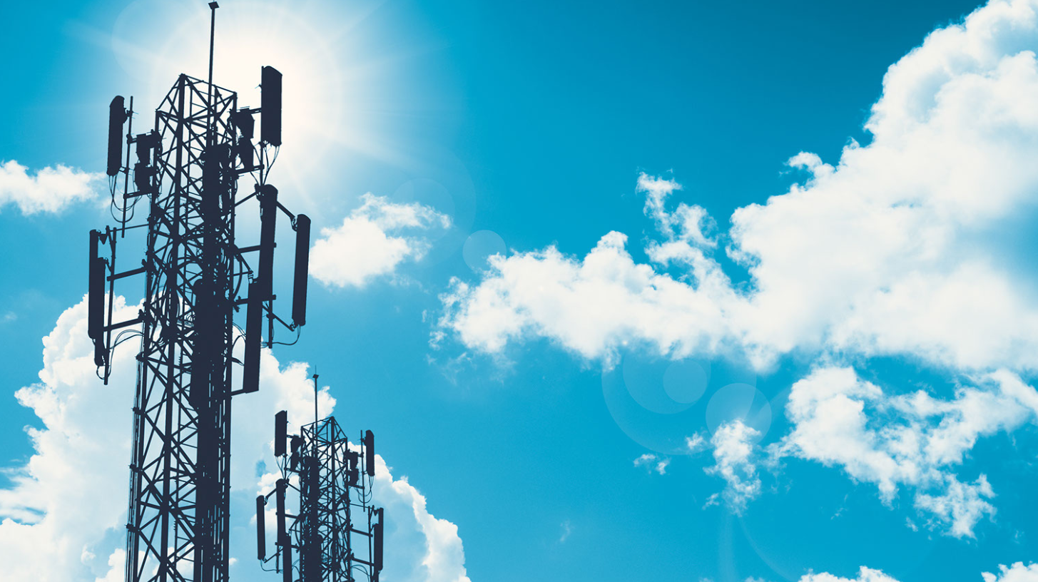 Decorative image of two cell towers in front of a sunny sky with wispy clouds.